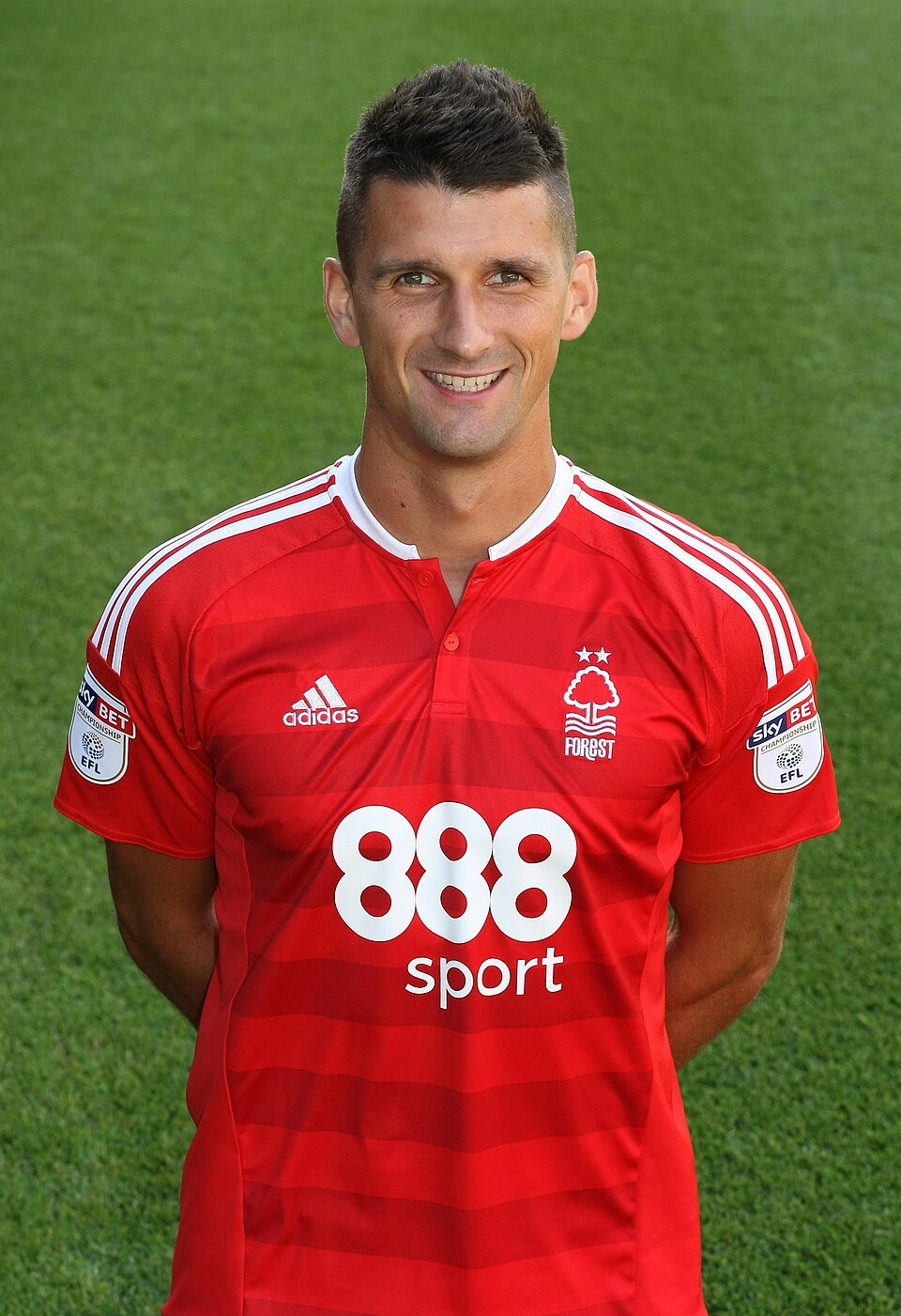 Eric Lichaj in a red Nottingham Forest football jersey, standing in front of a green pitch